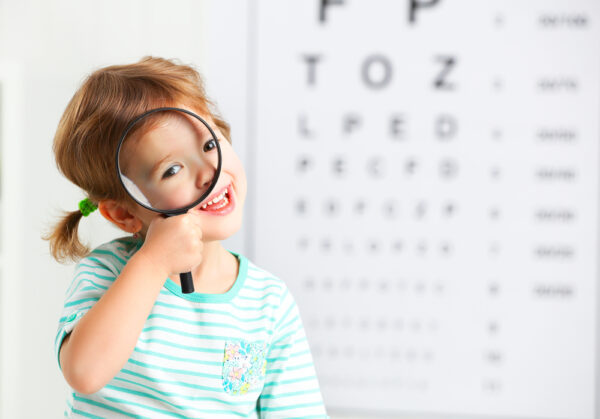 Cute girl looking through magnifying glass with eye chart in the background